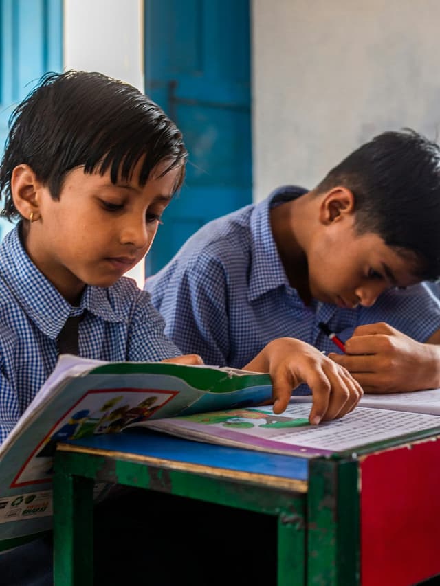Two school pupils in uniform working through a textbook together at their desk